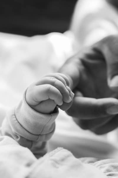The Best Pregnancy Books for Dad 2023 Featured Image. Image of newborn hand holding a mans finger.