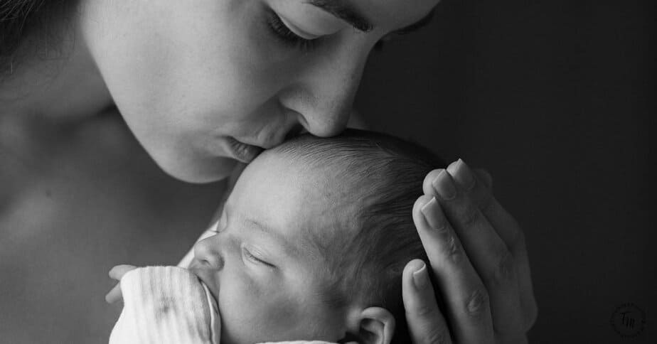 Postpartum Must-haves for new moms. Image of mom kissing new baby on head.