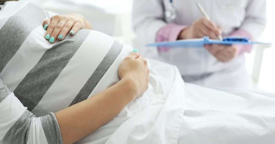 Pregnant woman lying on her back in a doctors office. Doctor in background. Fundal massage postpartum.