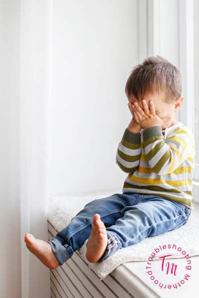 Toddler Power Struggle. Image: Toddler sitting on window seat with his hands covering his eyes. Toddler Discipline.