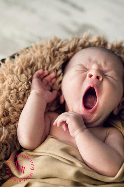 Baby yawning while lying on a soft blanket, representing waking up crying and common baby crying reasons during sleep