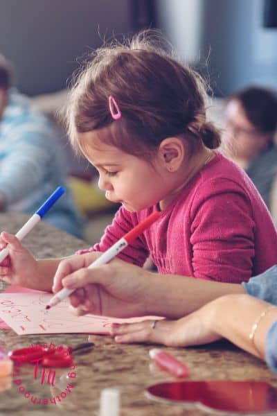 Child working on candy free Valentines for classroom exchange with markers and handmade cards