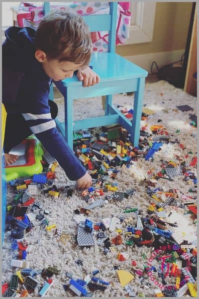 messy playroom floor covered in toys and legos while child plays, representing cleaning when kids destroy everything